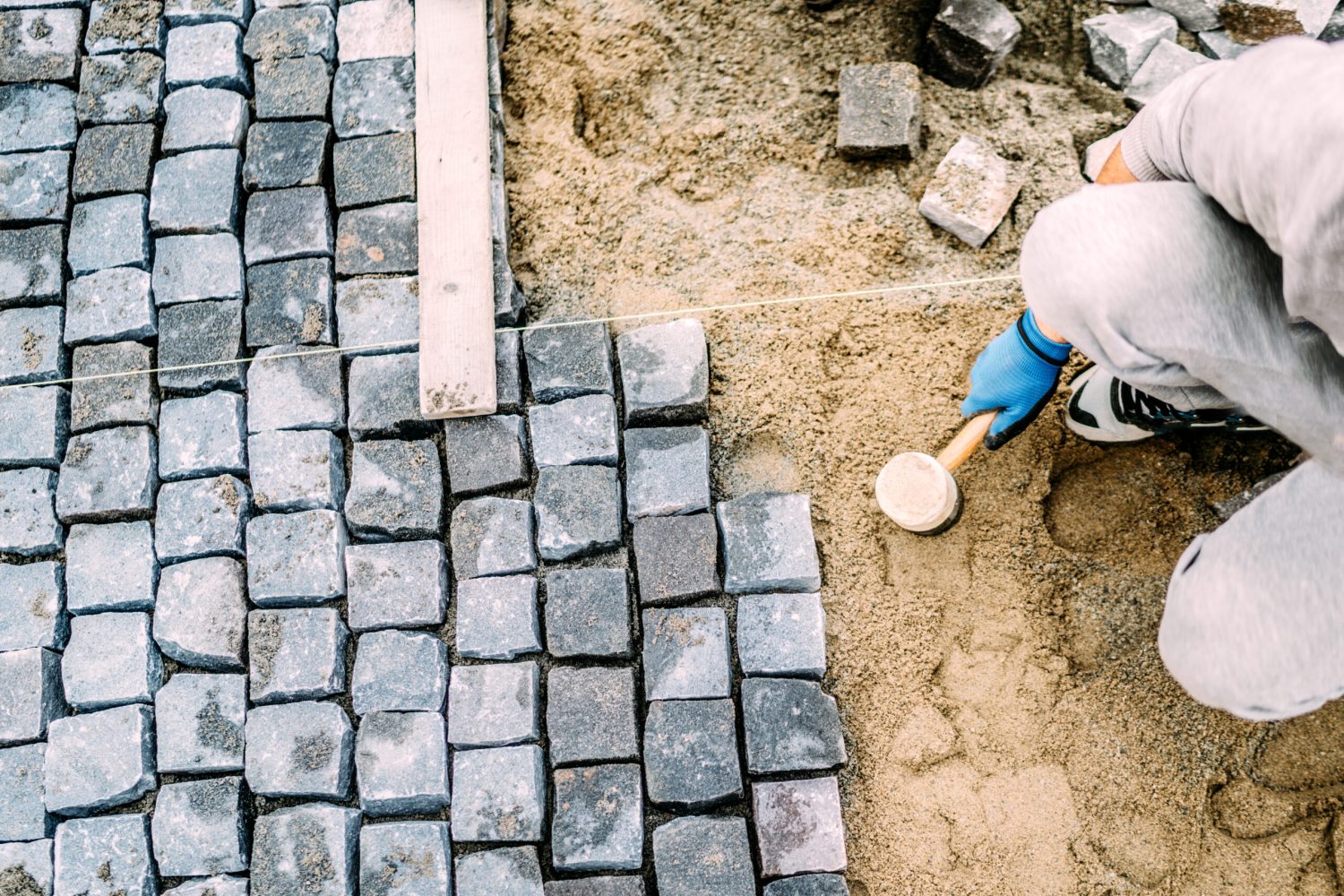 Manual labor, industrial worker laying stone pavement on sand path